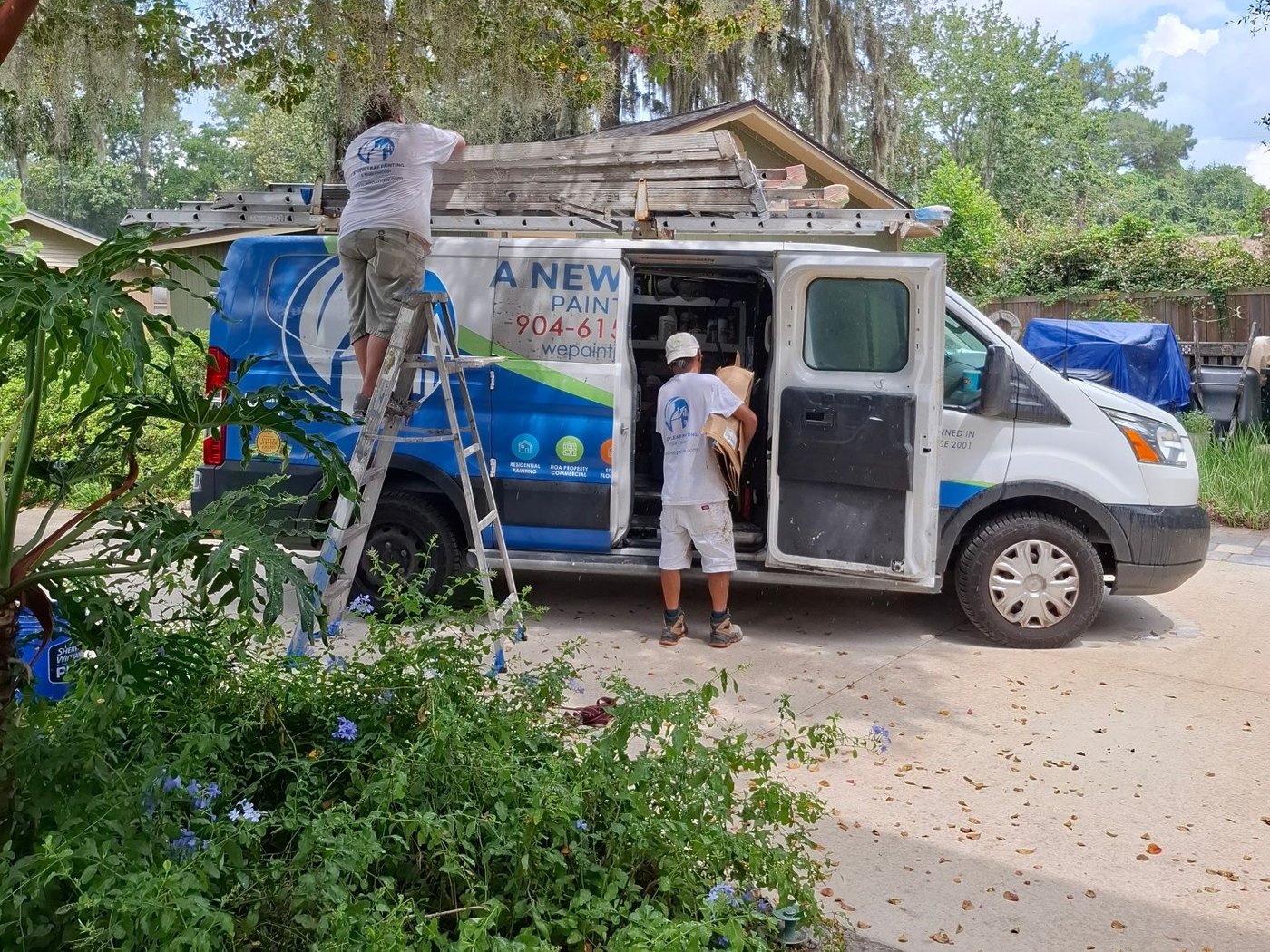 Two A New Leaf painters loading the company van under the oaks on a Jacksonville driveway