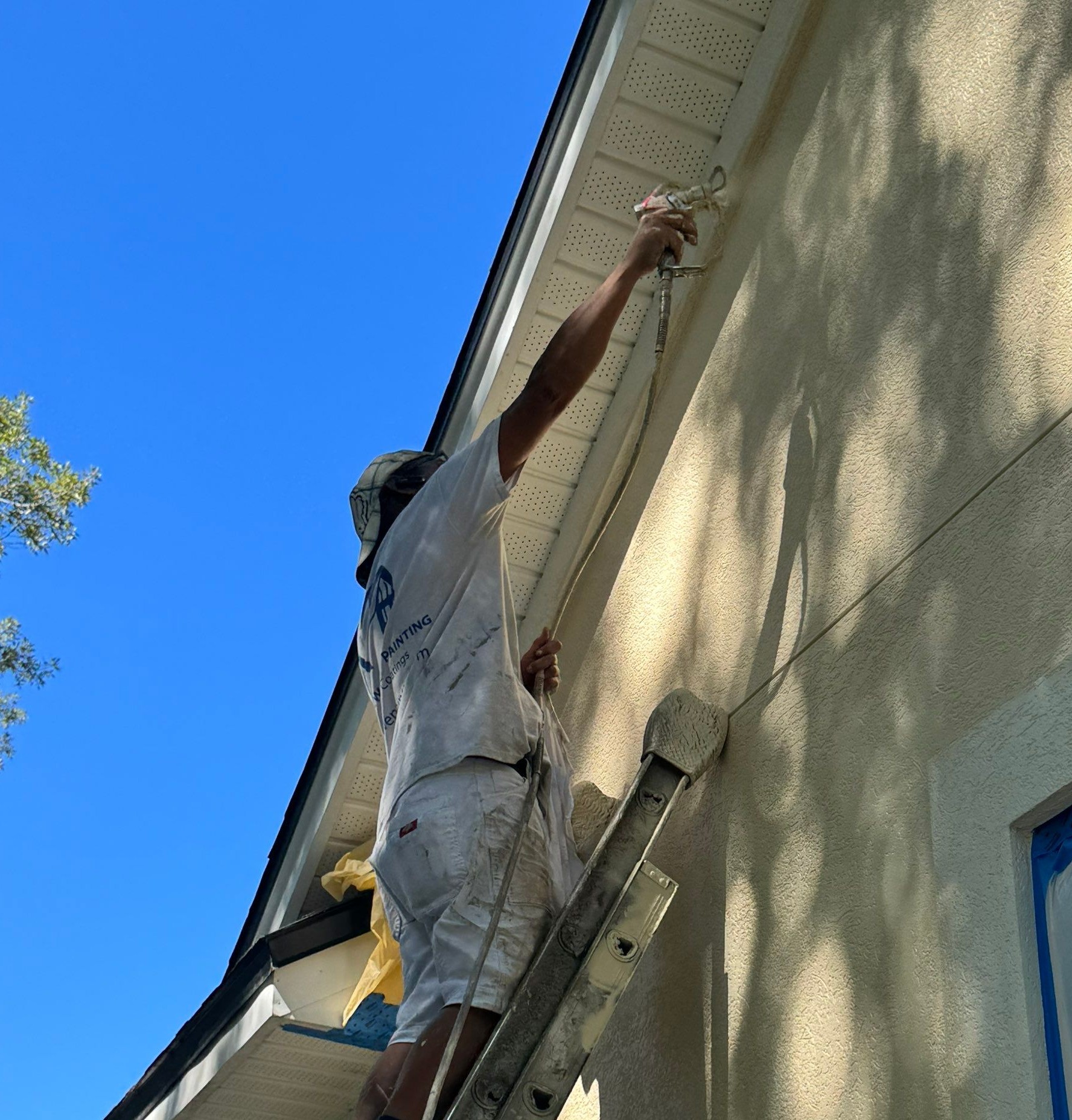 An A New Leaf painter on a ladder spraying the soffit line of a stucco home
